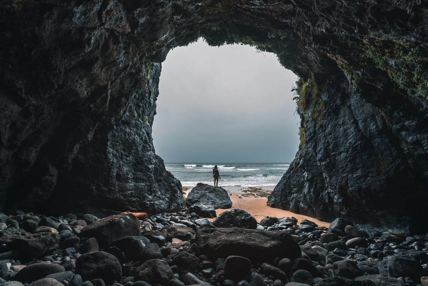 Blick aus einer Steinhöle hinaus. Der Ausgang ist riesig und vor der Höle ist das Strand und Meer zu sehen